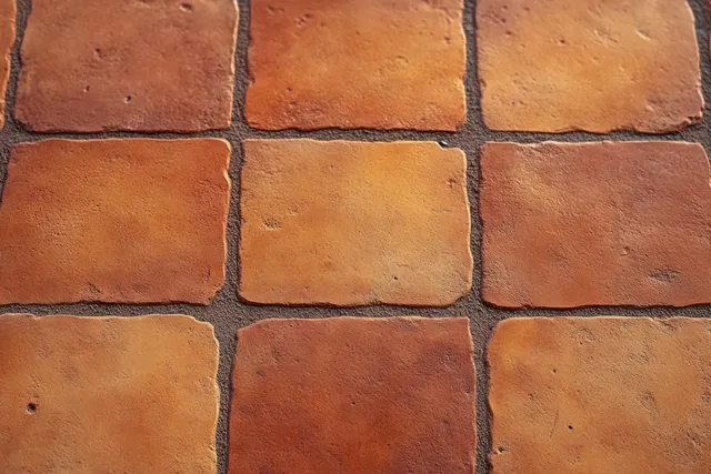 Square ceramic floor tiles in reddish brown with visible grout lines and a slightly textured surface.