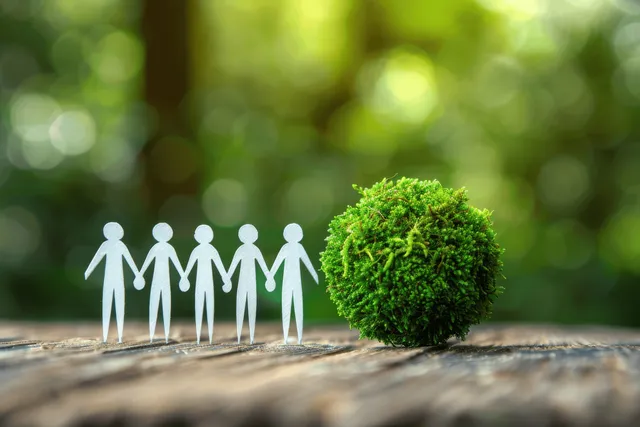 Paper people stand in a circle around a bright green Earth globe on a forest path.