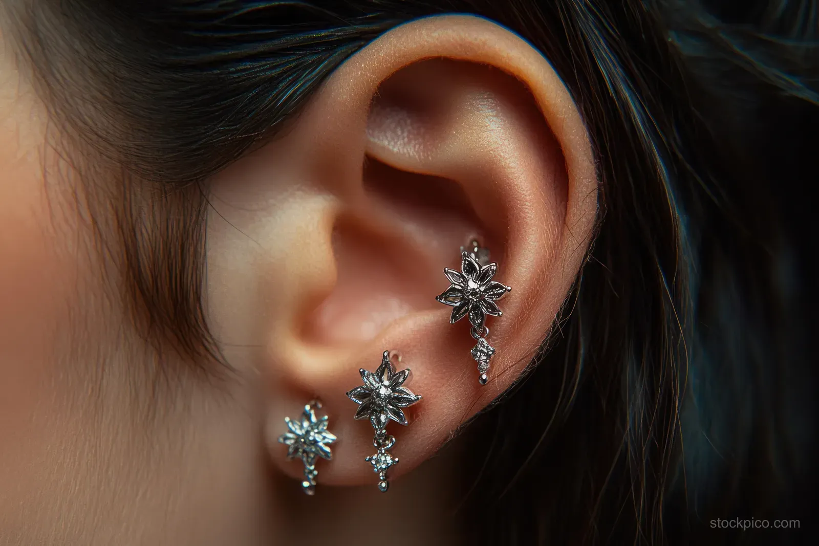 Close-up of an ear adorned with three silver floral earrings with intricate shiny details.