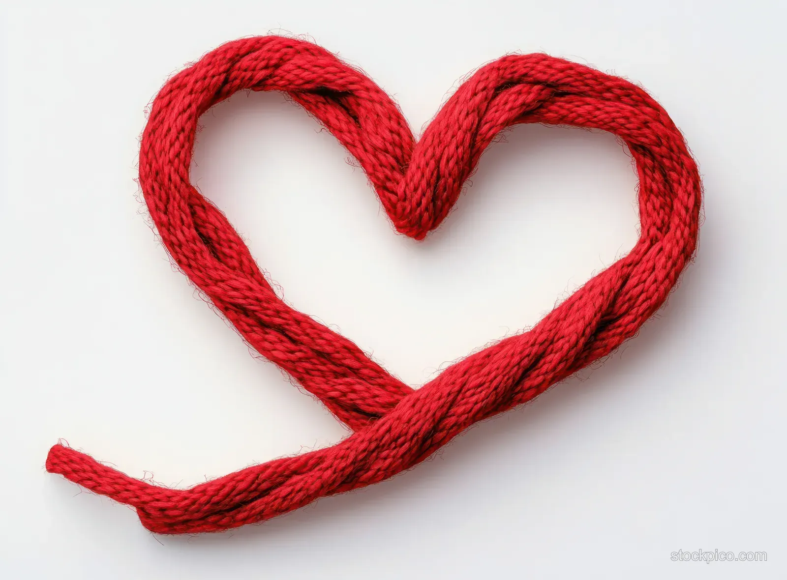 Red knitted yarn is shaped into a heart on a white background, showing the twisted fiber texture.