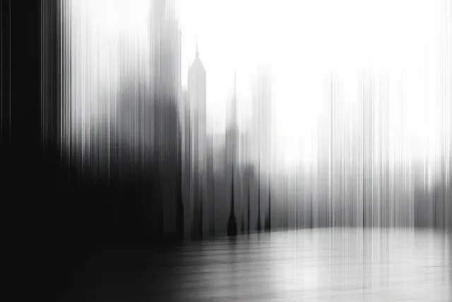 Blurred black-and-white skyline with tall buildings and a hazy reflection across still water.