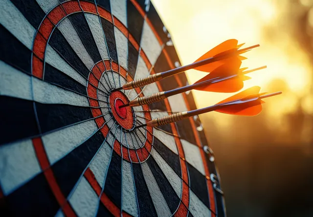 An orange dart is embedded in the bullseye of a dartboard with warm sunlit background blur.