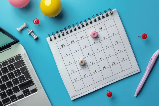 Calendar pinned with red markers beside open laptop on blue planning desk