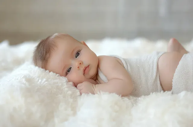 Peaceful baby lying on a soft white blanket, calmly gazing at the camera indoors
