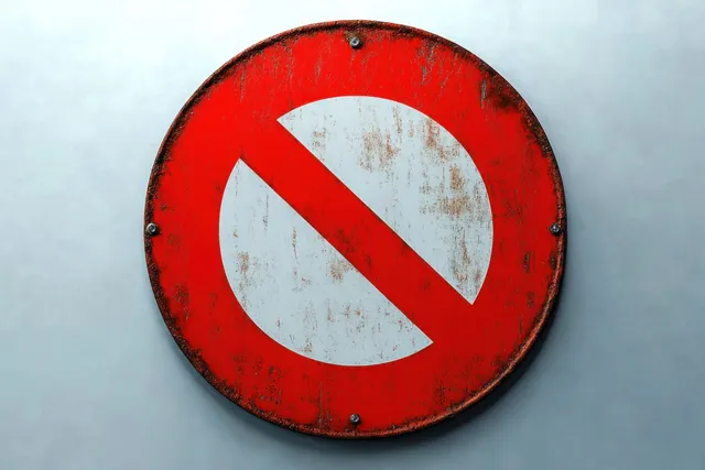 A rusty red and white No Entry sign is bolted to a pale gray wall.