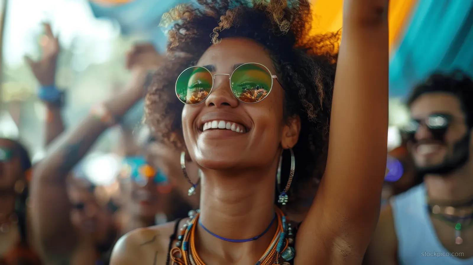 Smiling young festivalgoer dancing outdoors in sunlight with colorful sunglasses and a raised arm.
