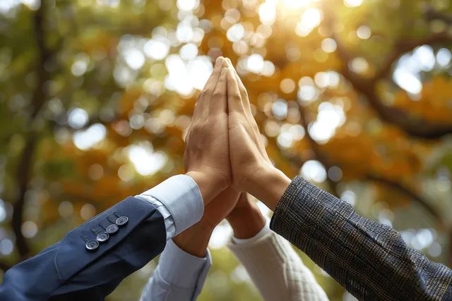 Hands joined in prayer pose outdoors, sunlight bokeh suggesting environmental unity
