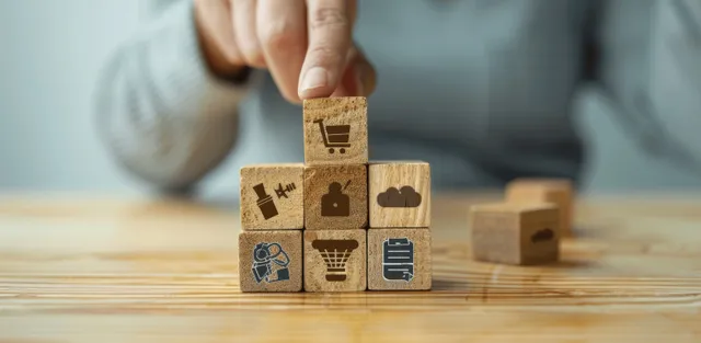 A hand stacks wooden blocks with icons on a table, representing employee benefits and compensation.