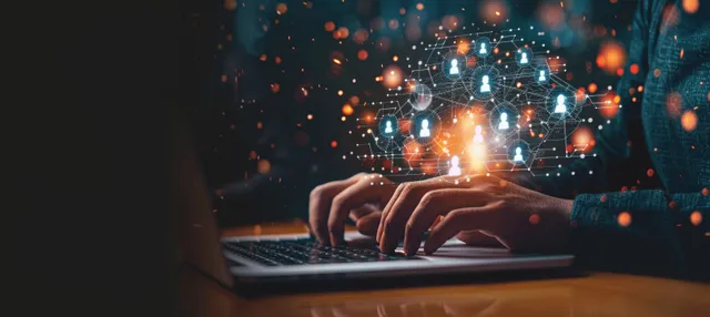 A person types on a laptop while glowing holographic social media icons and network connections float overhead.