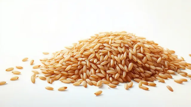 Uncooked brown rice grains are scattered in a pile on a white surface.