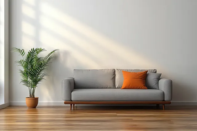 Minimalist living room corner with gray sofa, orange pillow, and green potted plant