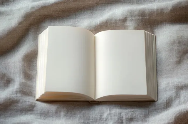 An open blank book with empty white pages lies on textured fabric under soft natural light.