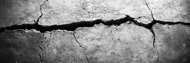 Monochrome close-up of a cracked concrete wall with branching fractures and rough weathered texture.