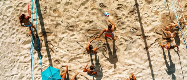 Women beach volleyball players jump at the net on a sandy court during a fast rally.