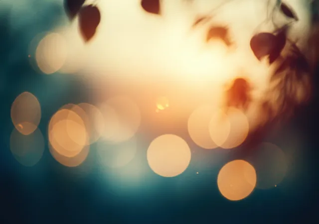 Glowing golden bokeh circles blur across a soft blue background with a warm vintage glow.