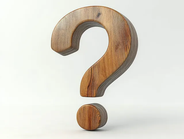 A carved wooden question mark symbol with visible timber grain on a light background.