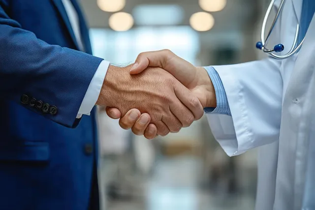 A businessman and doctor shake hands in a hospital lobby during a professional healthcare meeting.