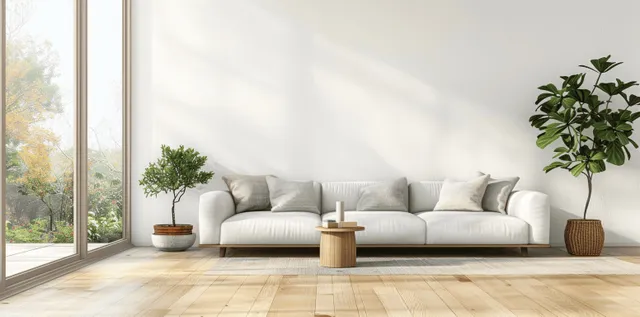 A white sofa sits on light wooden floor beneath a large window with visible greenery outside.