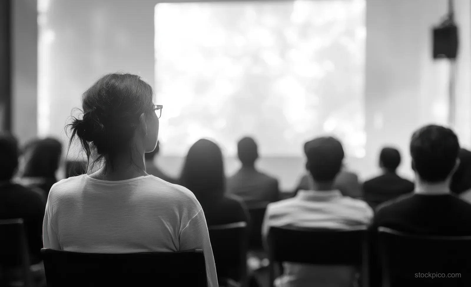An attendee stands facing a seated audience during a corporate seminar presentation in soft, modern art lighting.