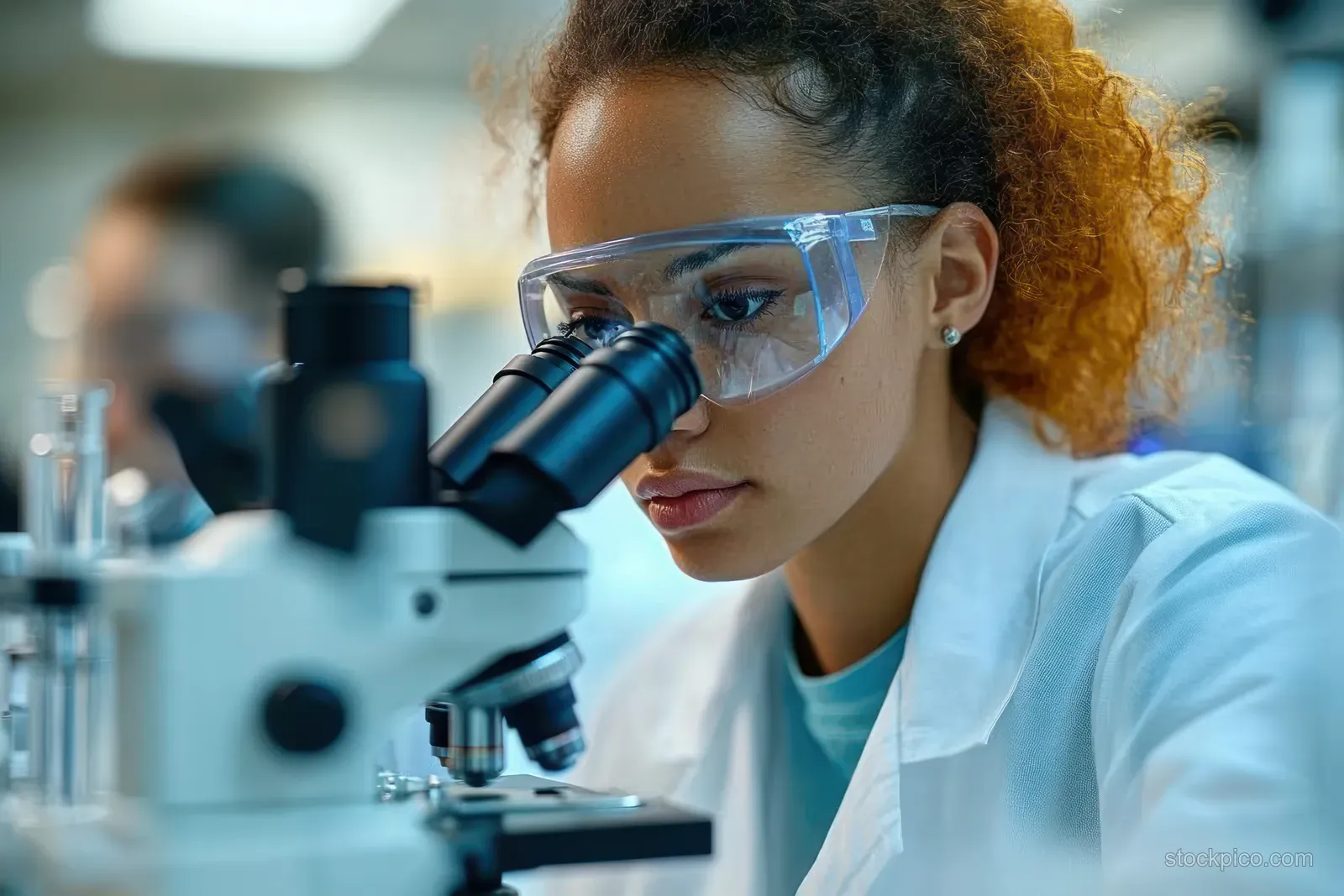 African American scientist observes samples through a microscope in a bright laboratory with other instruments blurred behind.