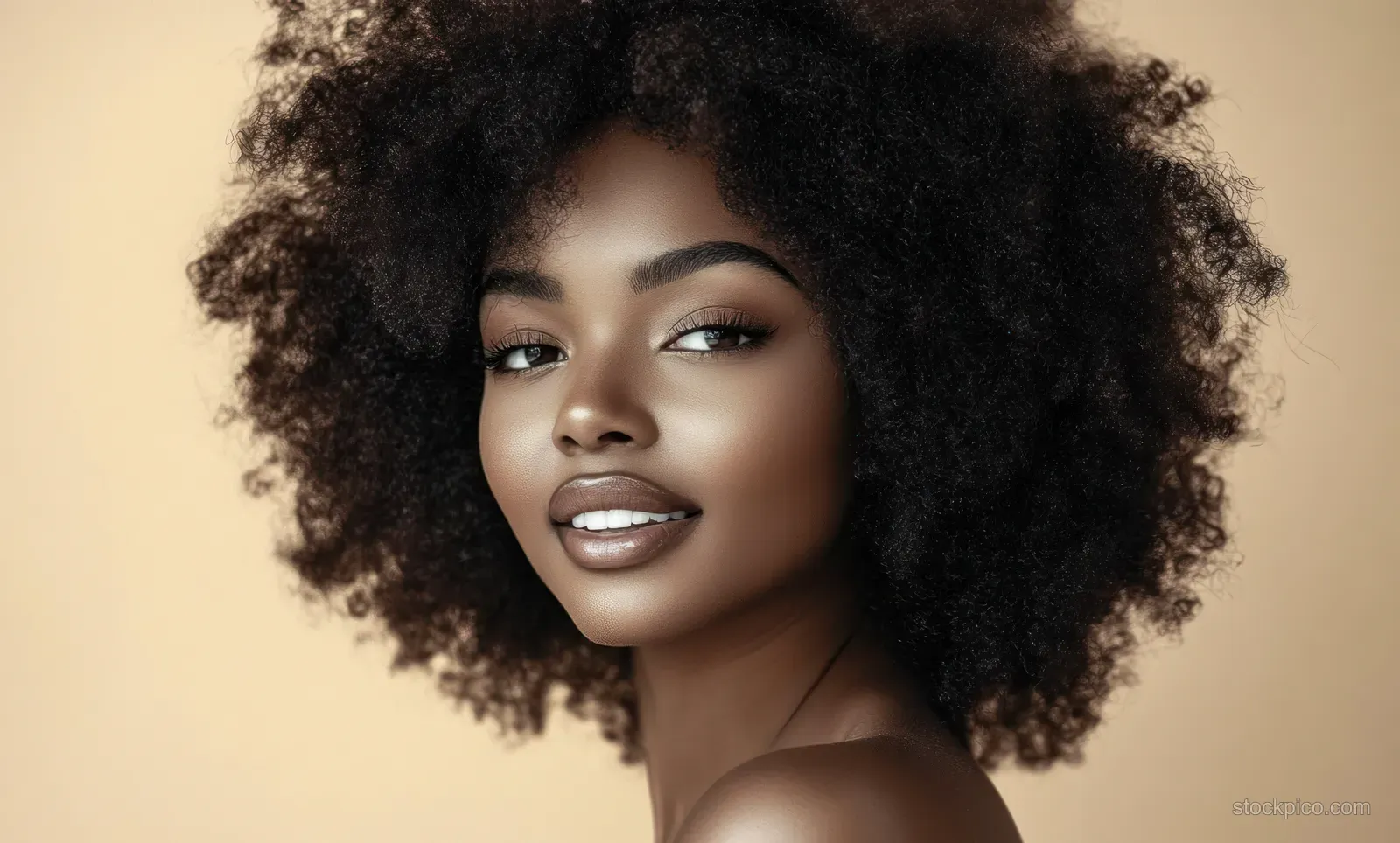 Close-up portrait of a smiling woman with natural curly afro hair and smooth skin against a warm beige background.