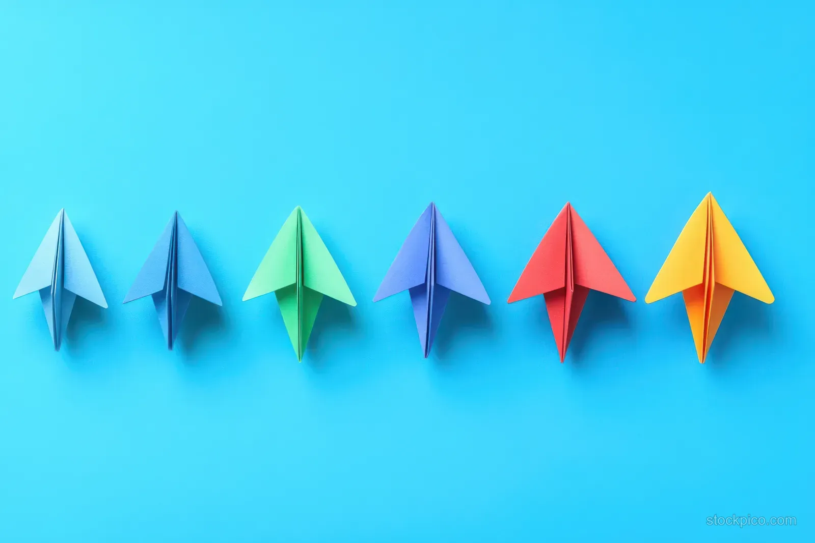 Colorful paper airplanes are arranged in a line on a blue background.