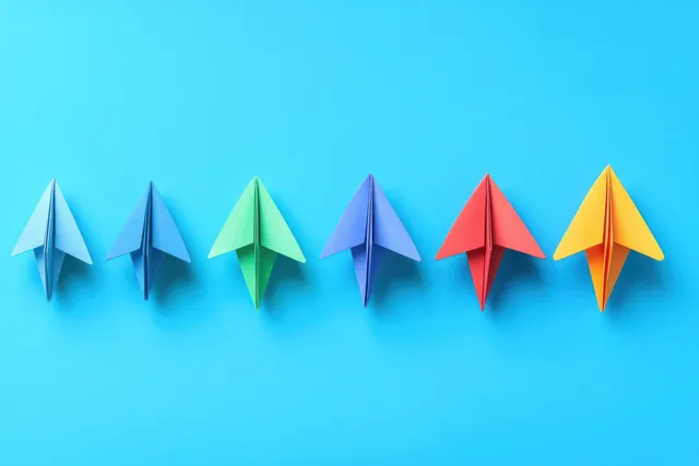 Colorful paper airplanes are arranged in a line on a blue background.