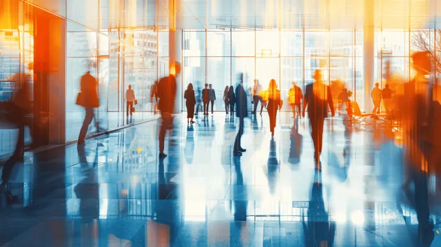 Blurred professionals walk across a modern office lobby floor under panoramic windows with city light streaming in.