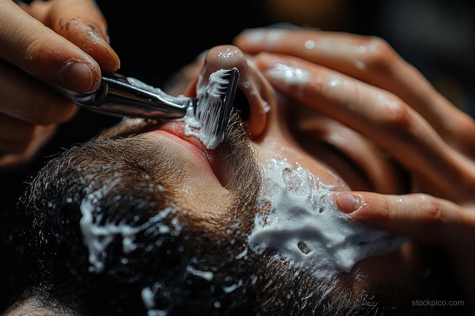A man holds a shaving brush while lather covers his beard and wet face during shaving.