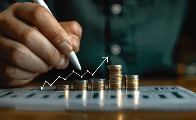 Hand adjusting rising stock chart above stacked coins on financial desk