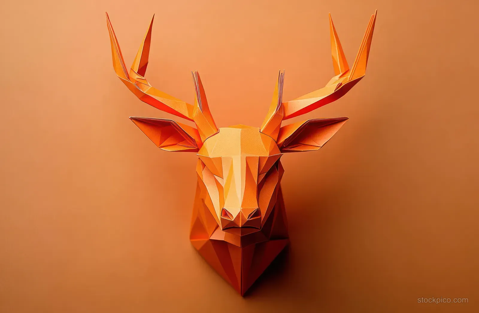 Faceted low-poly paper deer head with tall antlers displayed on a solid orange background.