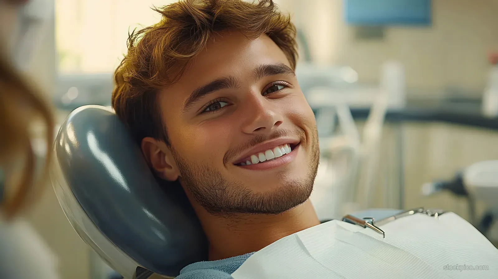 A smiling young man reclines in a dentist chair during a dental checkup in a bright clinic.