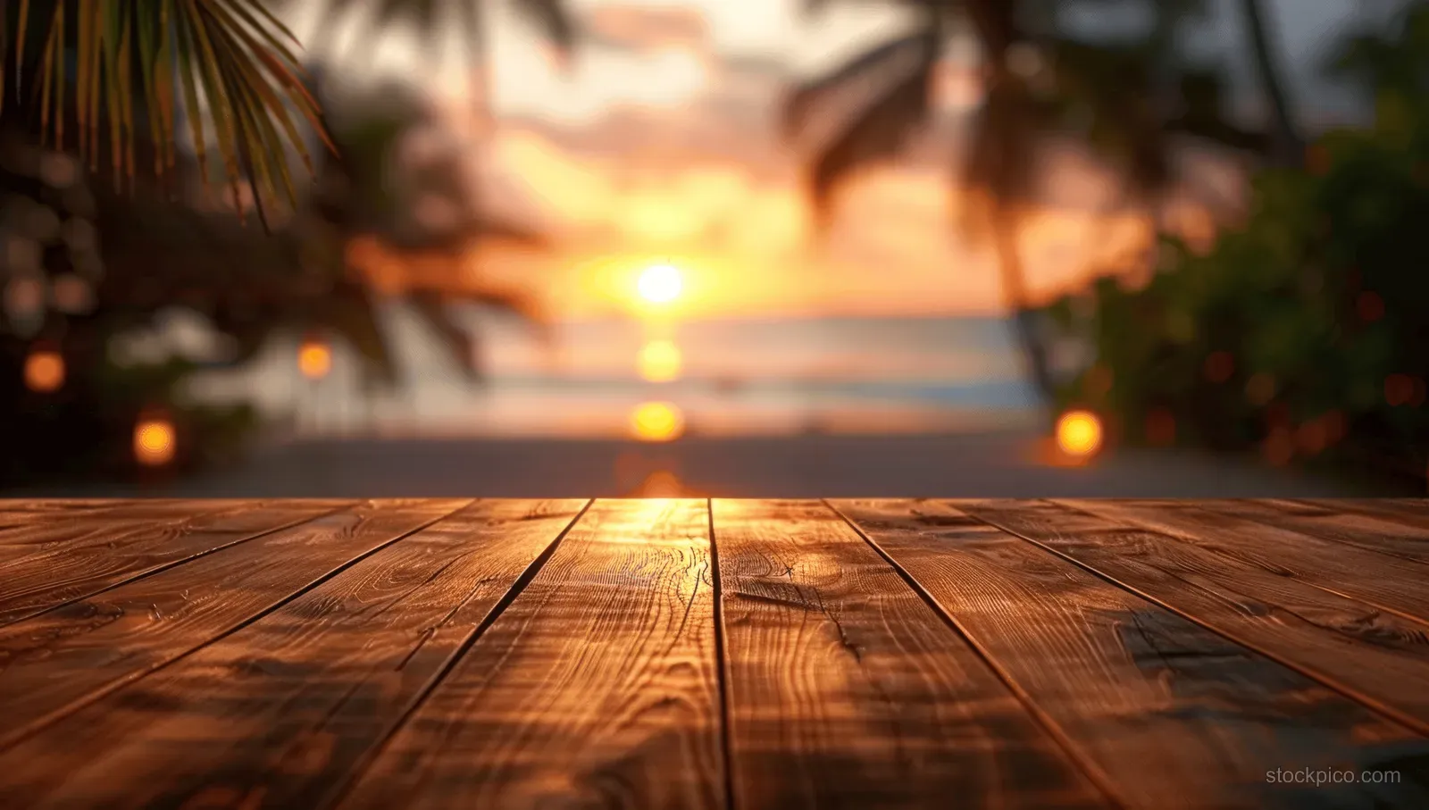 A wooden deck in the foreground frames a tropical beach sunset with palm trees and a glowing ocean horizon.
