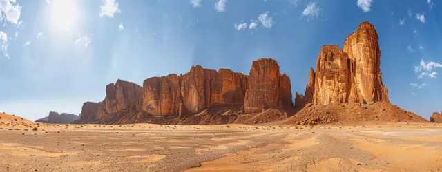 Panoramic sandy desert landscape with towering Al Hafr sandstone rock formations under a bright blue sky.