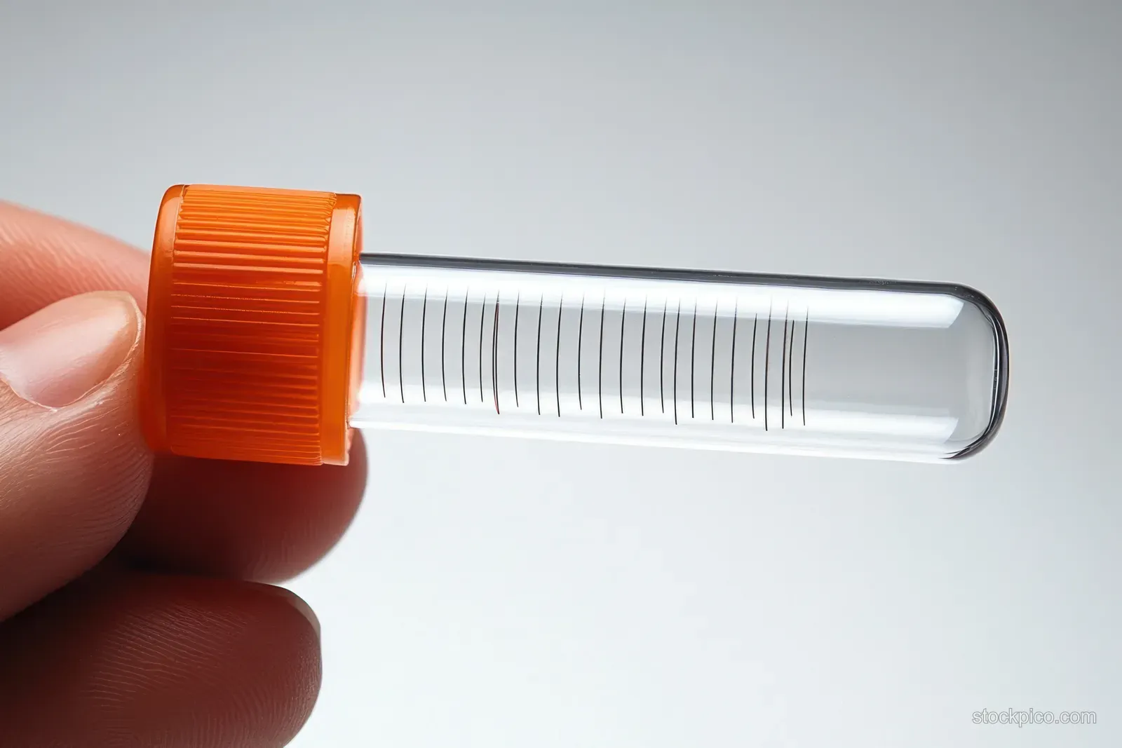 A hand holds a small clear plastic test tube with an orange screw cap and visible measurement markings.