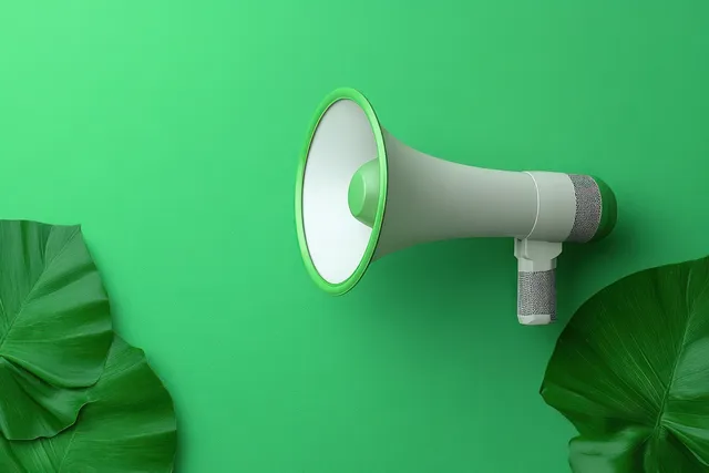 Wall-mounted gray megaphone on a green wall with tropical leaf decorations on both sides.