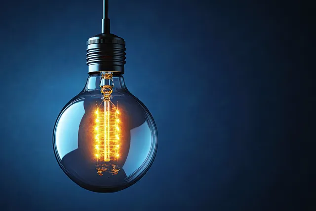 Glowing incandescent light bulb with visible filament hanging against a deep blue backdrop