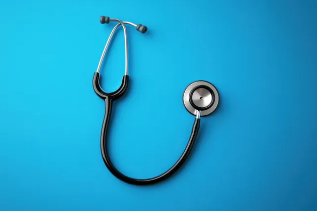 Black and silver stethoscope placed on a vibrant blue background with its round chest piece visible.
