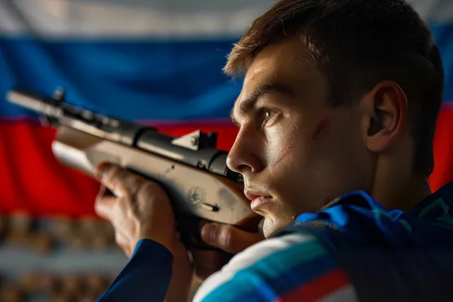 A Russian air pistol shooter aims an air pistol at a 10m target beside blue and red flags.