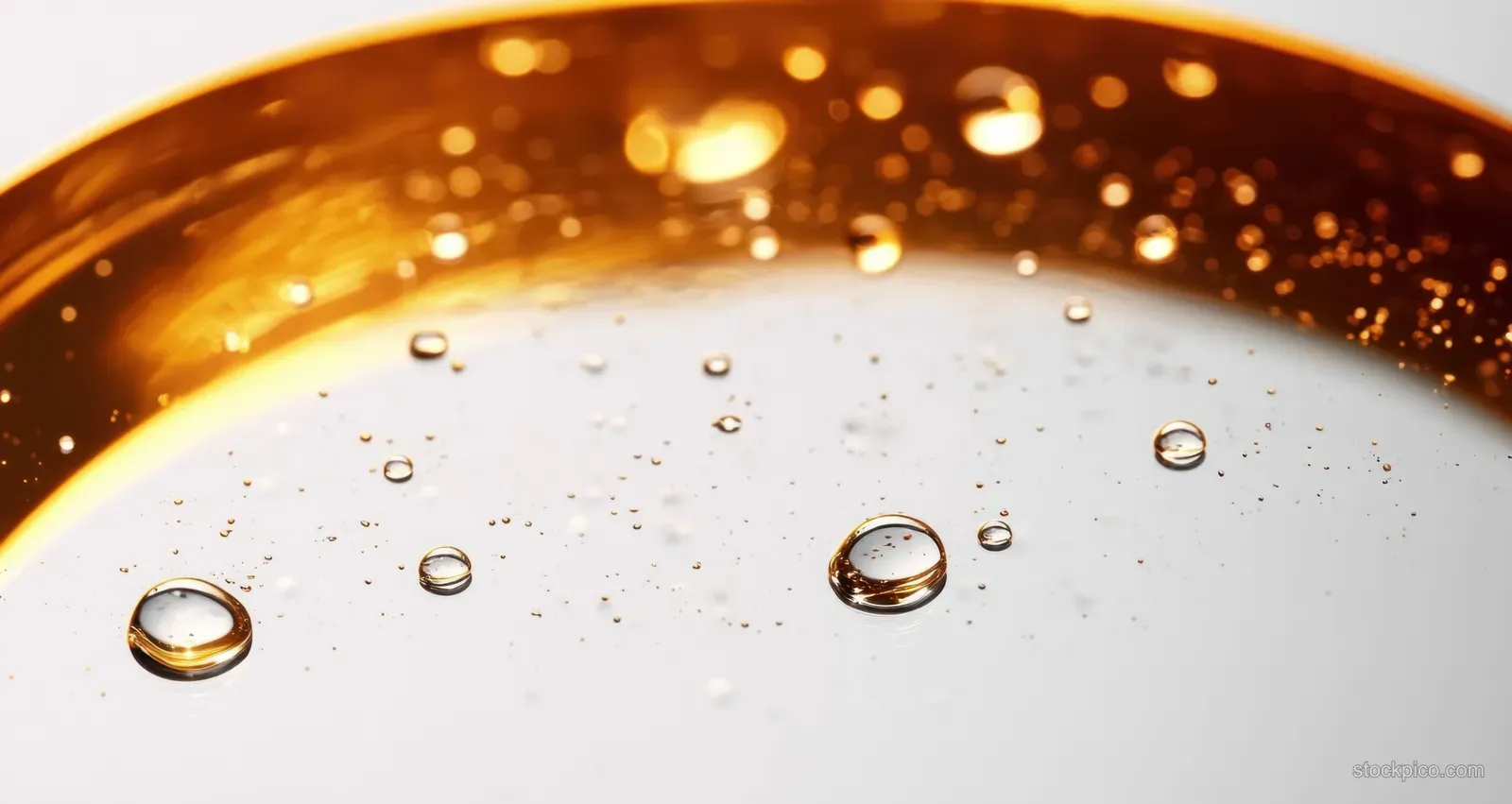 Close-up of a golden liquid surface with small bubbles suspended in a clear fluid under soft light.