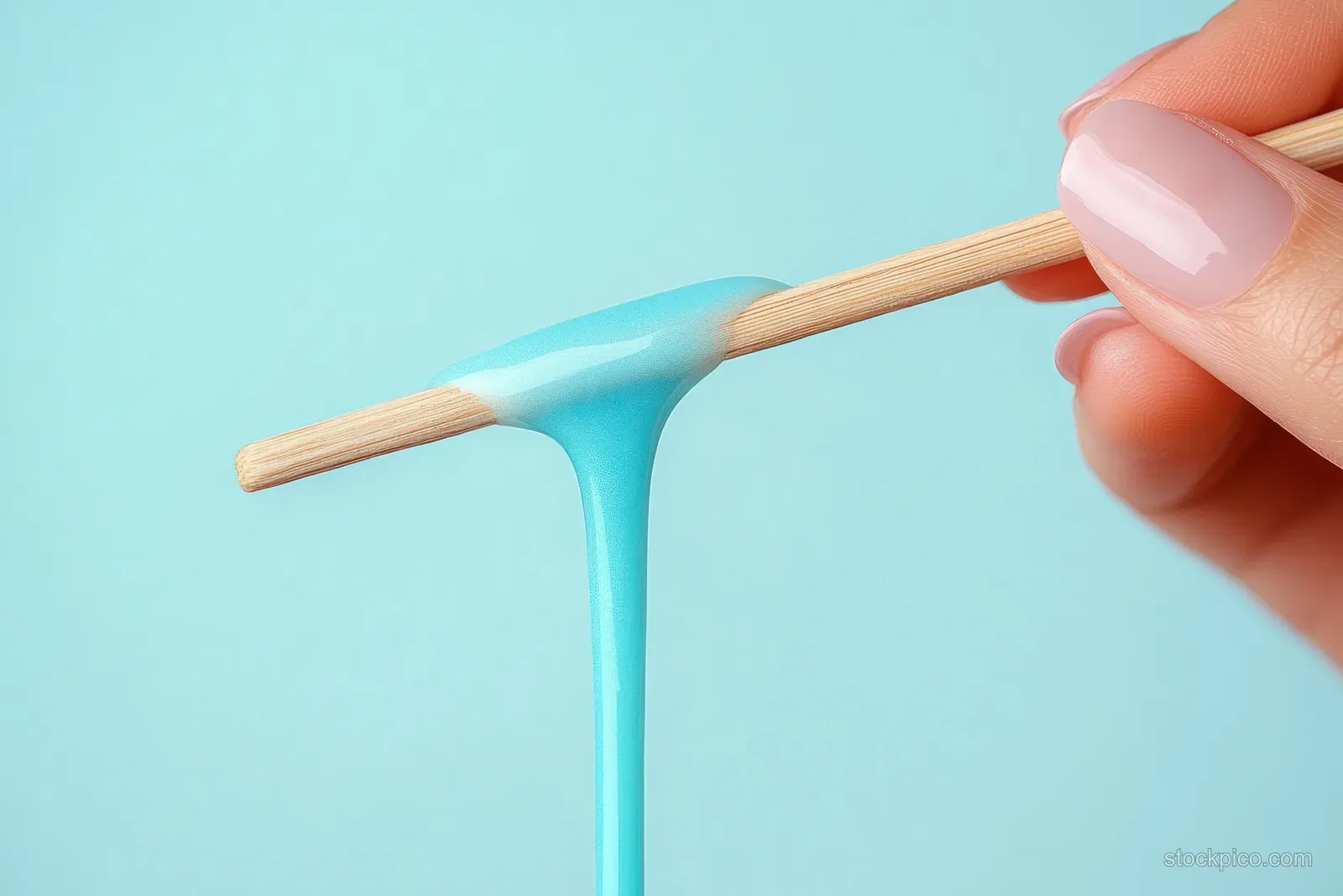 A hand holds a wooden stick with wax dripping into a container on a blue background.