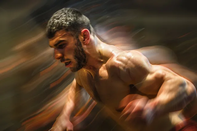 Turkish wrestler holds an opponent in a freestyle grappling match with dramatic motion blur in the background.