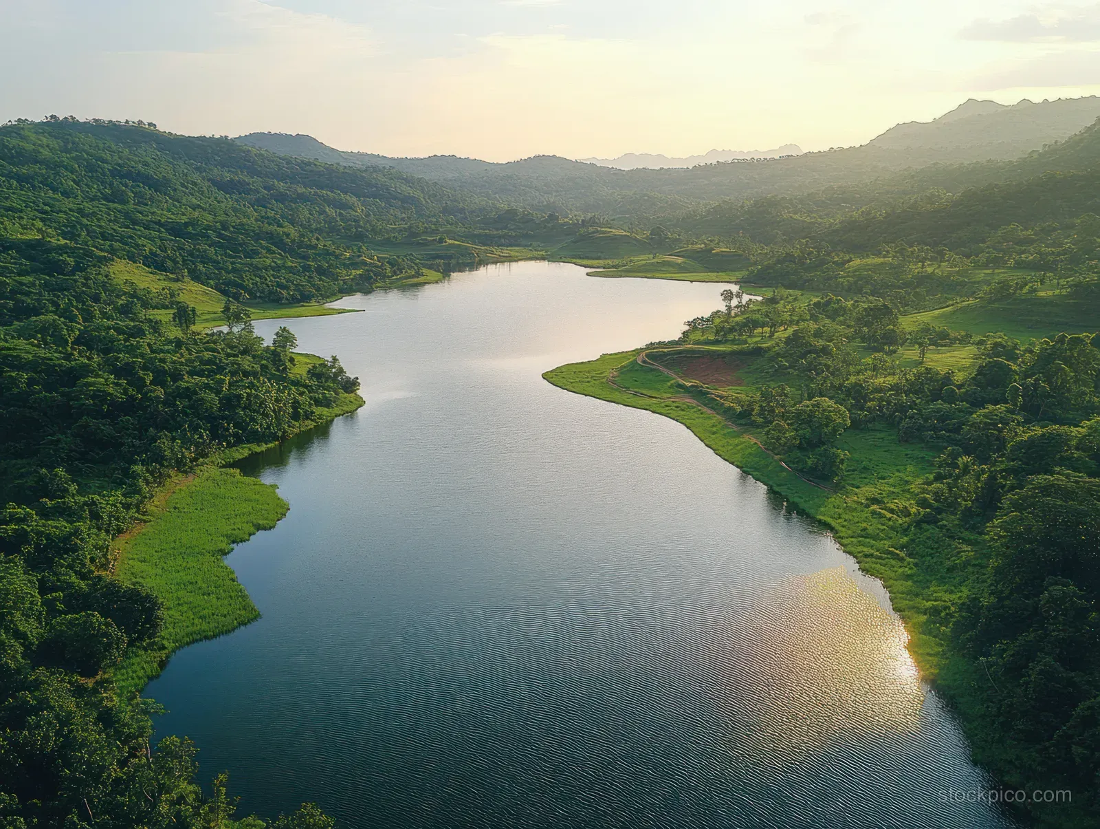 Drone aerial view of Sermo Lake winding through lush green hills under soft sunrise light.