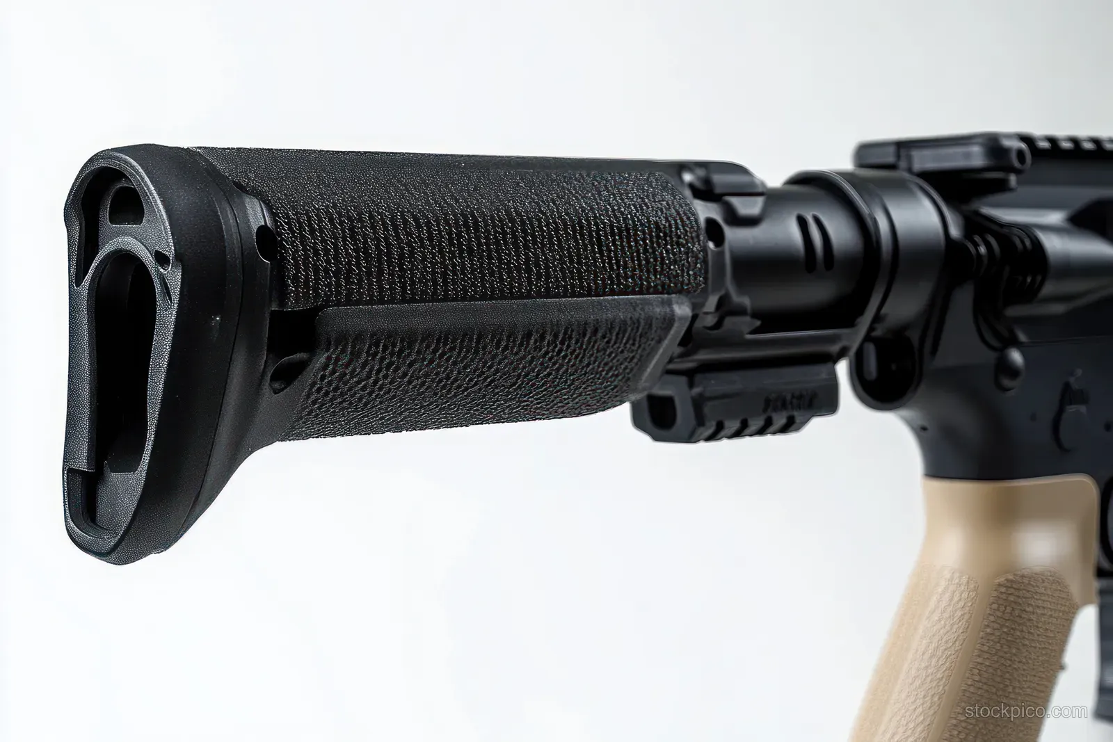 Close-up of a tactical rifle stock and textured grip with matte black and tan parts on a plain white background.