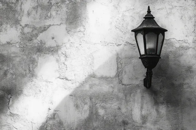 A vintage outdoor wall lantern casts sharp shadows on a weathered monochrome plaster wall.