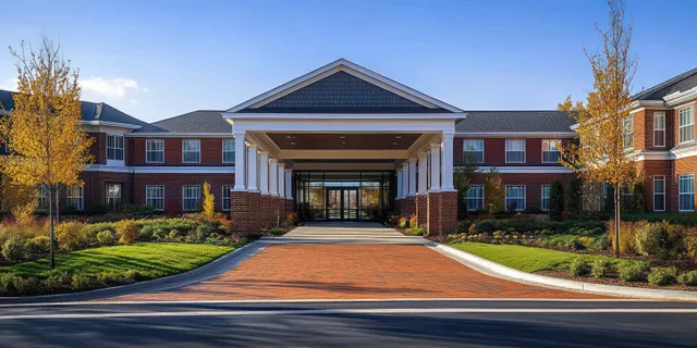 Red brick institutional building with white columns and a covered entrance, landscaped yard