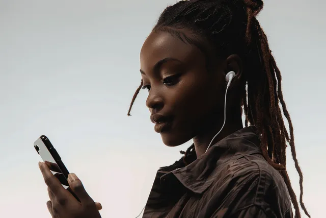 Young woman with dreadlocks listens via earbuds while looking at smartphone