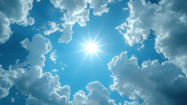 Sun shining through scattered fluffy clouds in a panoramic blue summer sky with visible light rays.