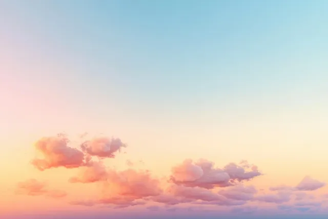 Pastel sunset sky with scattered fluffy clouds glowing in warm pink and orange hues