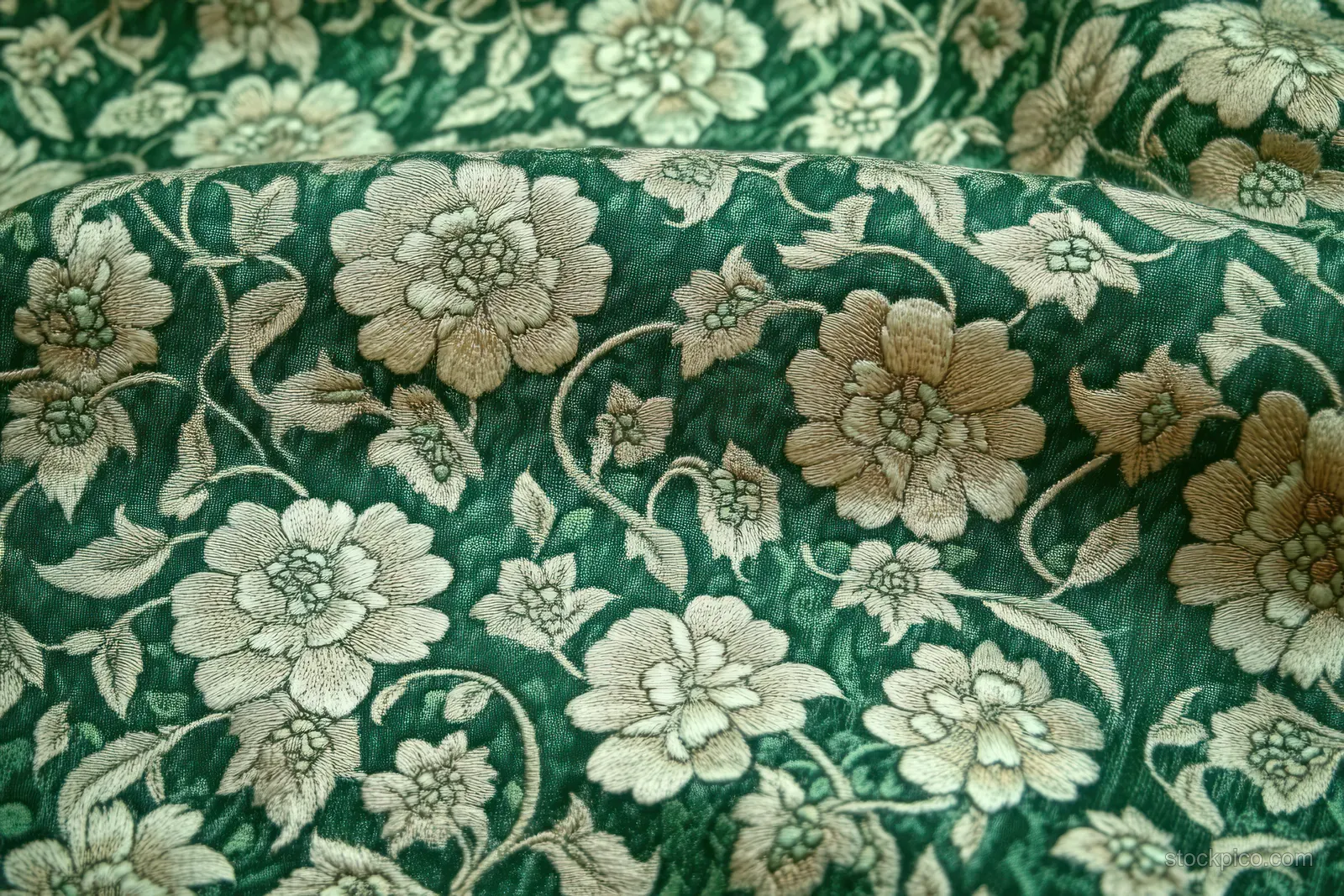 Textured green fabric with beige floral embroidery of stitched flowers and swirling stems fills the frame.